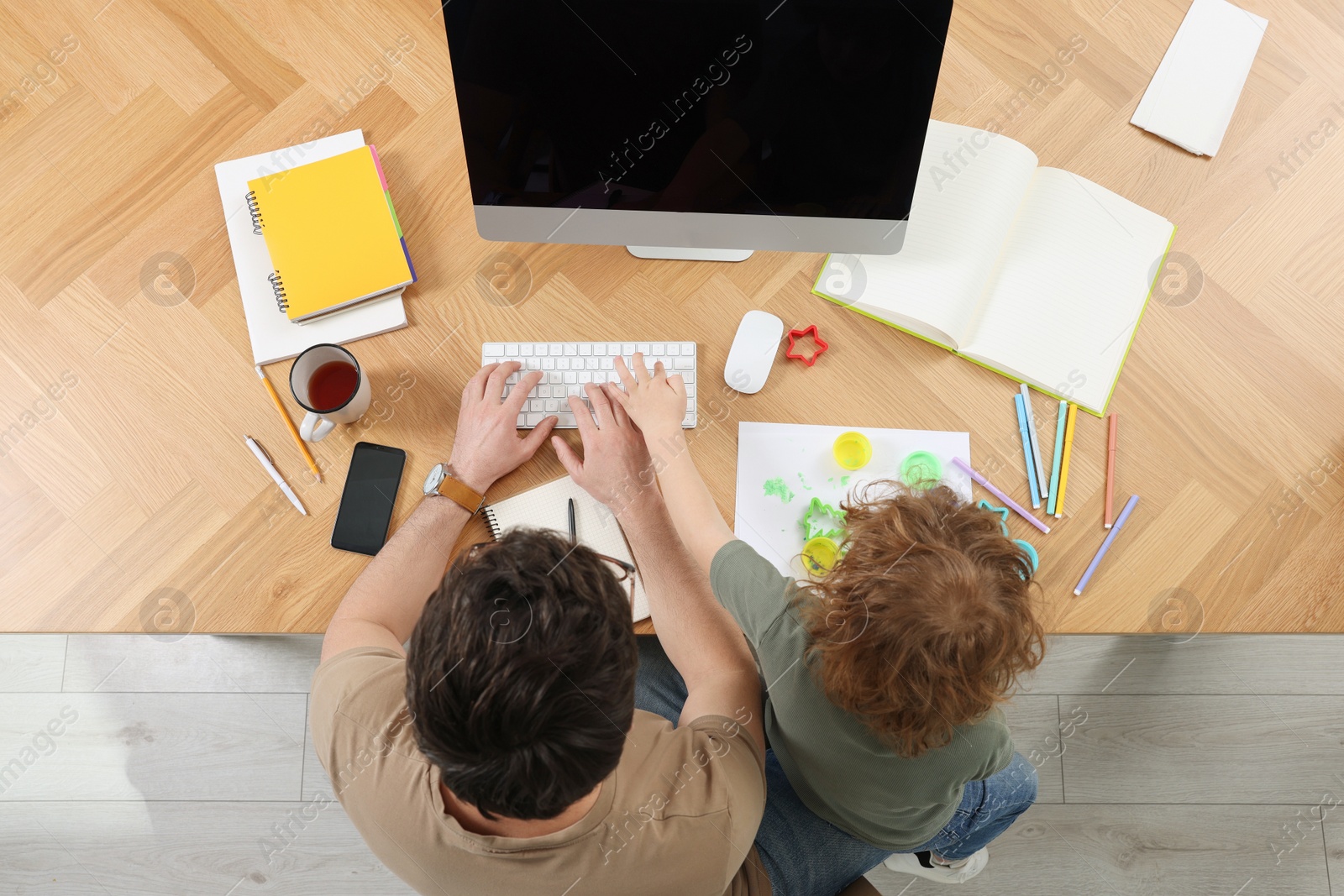 Photo of Little boy bothering his father at desk, top view. Man working remotely at home