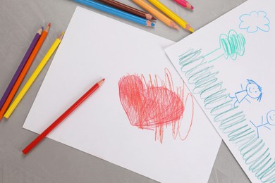 Photo of Cute children`s drawings and colorful pencils on grey table, flat lay