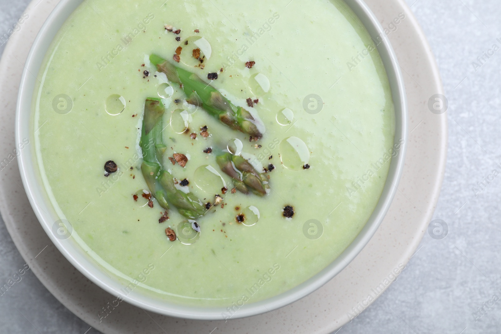Photo of Delicious asparagus soup on light grey table, top view