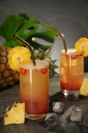 Photo of Glasses of tasty pineapple cocktail, sliced fruit and ice cubes on grey table