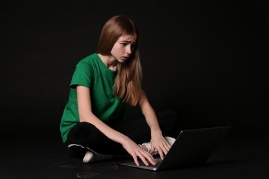 Photo of Shocked teenage girl with laptop on black background. Danger of internet