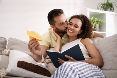 Photo of Happy man playing with paper plane while his girlfriend reading book in living room, focus on hand
