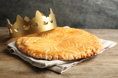 Photo of Traditional galette des Rois with paper crown on wooden table