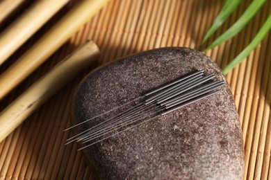 Stone with acupuncture needles on bamboo mat, above view
