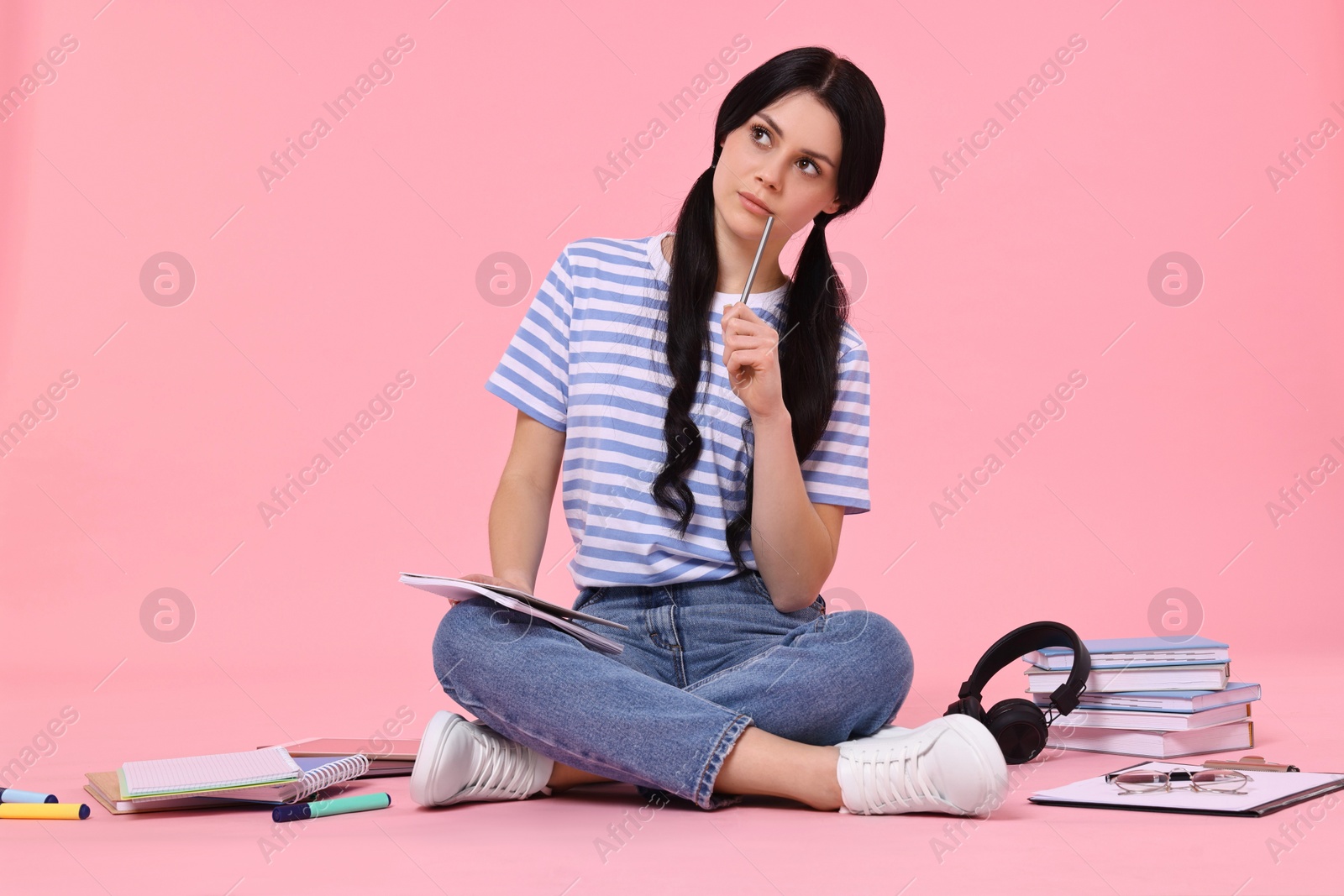 Photo of Student with notebook sitting among books and stationery on pink background