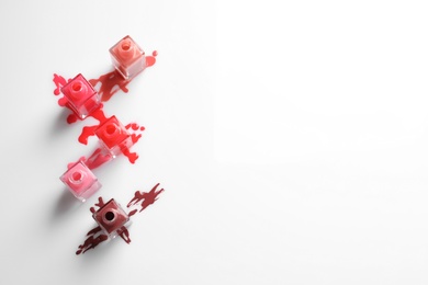 Photo of Spilled different nail polishes with bottles on white background, top view