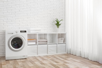 Photo of Modern washing machine near brick wall in laundry room interior, space for text