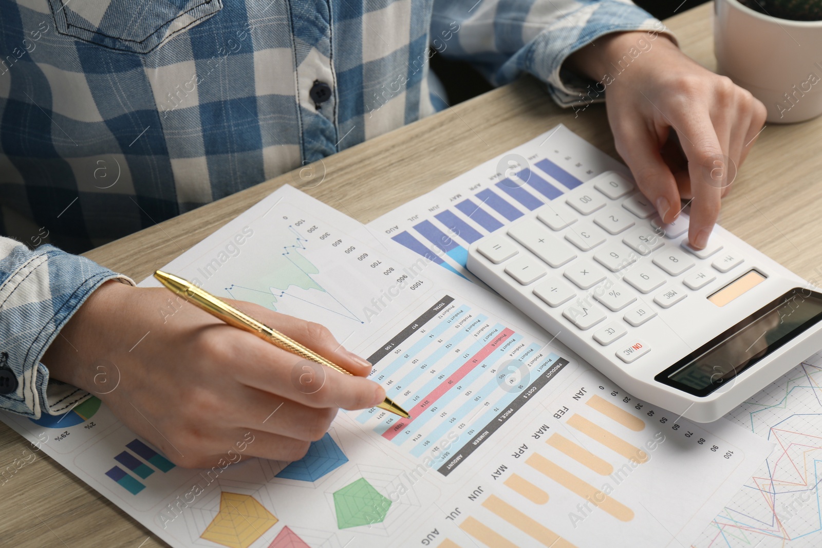 Photo of Woman using calculator while working with accounting documents at wooden table, closeup