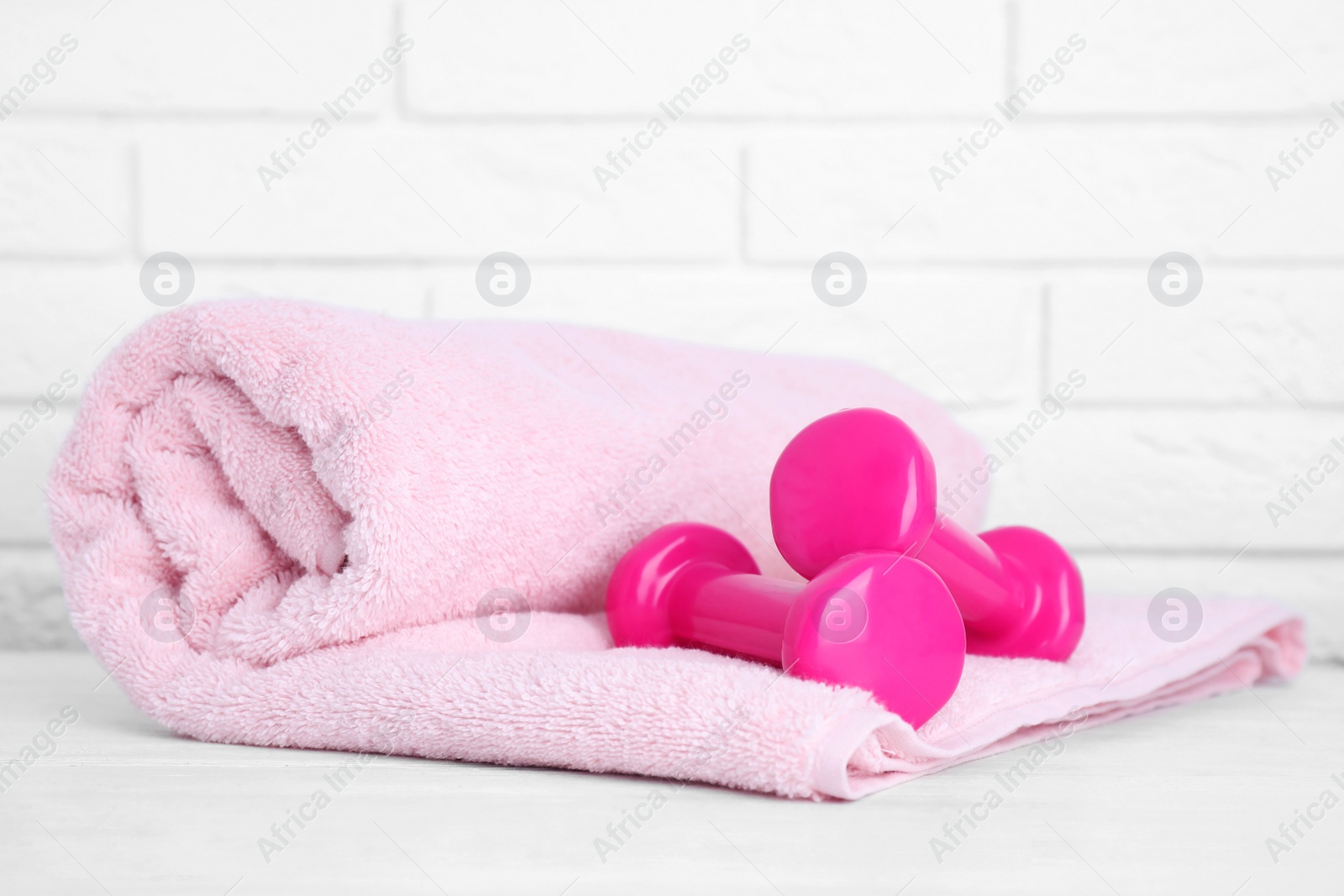 Photo of Stylish dumbbells and towel on table against brick wall, space for text. Home fitness