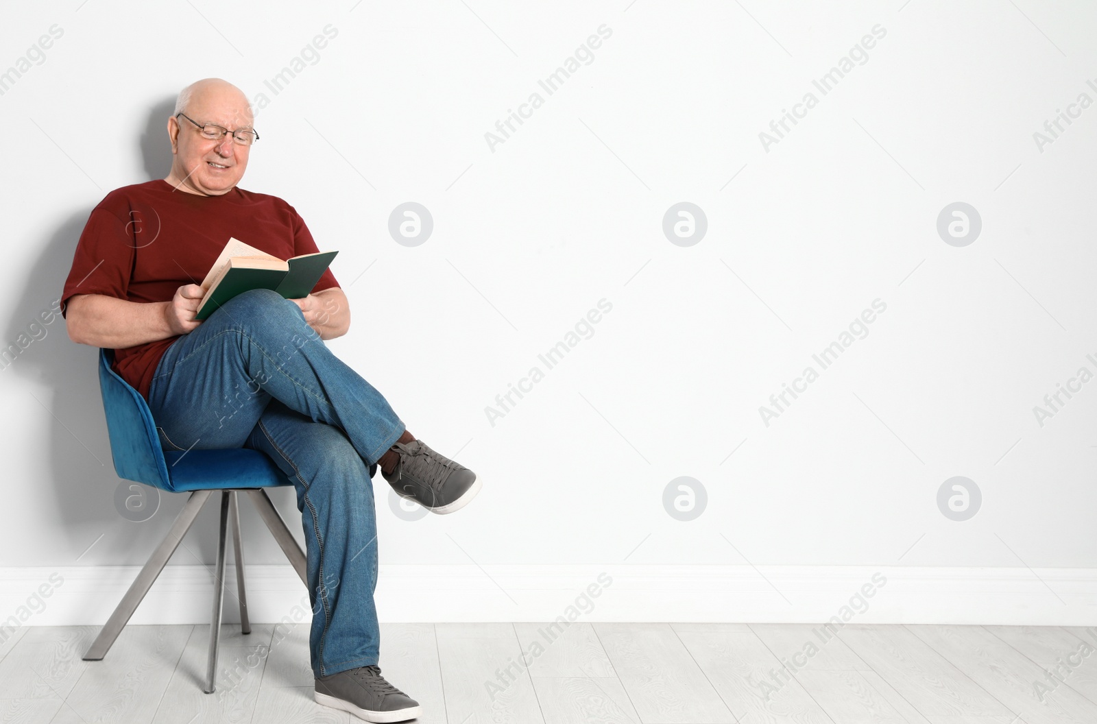 Photo of Portrait of senior man with glasses reading book near light wall. Space for text
