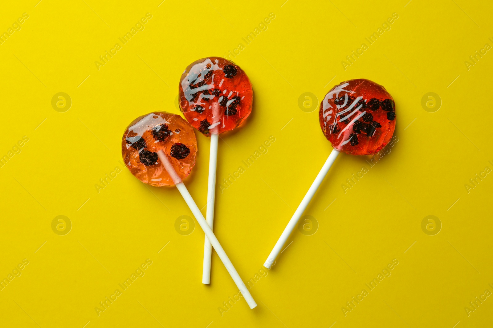 Photo of Sweet colorful lollipops with berries on yellow background, flat lay