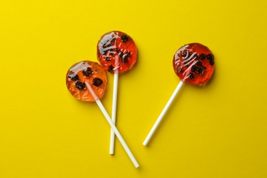 Sweet colorful lollipops with berries on yellow background, flat lay