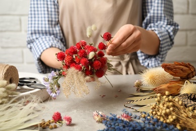 Florist making bouquet of dried flowers at light grey table, closeup