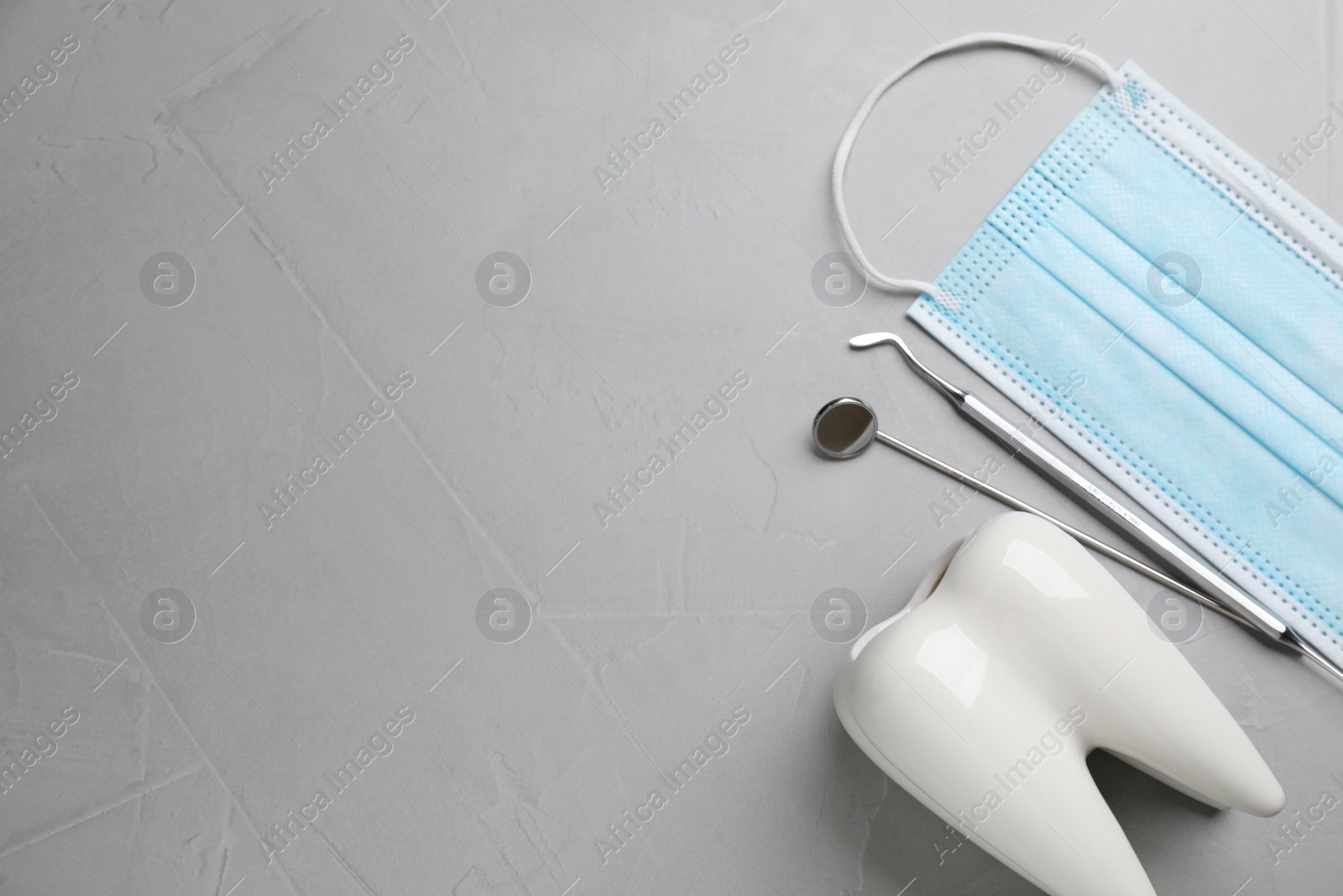 Photo of Tooth shaped holder, dentist's tools and face mask on grey table, flat lay. Space for text