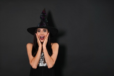 Photo of Excited woman wearing witch costume for Halloween party on black background, space for text