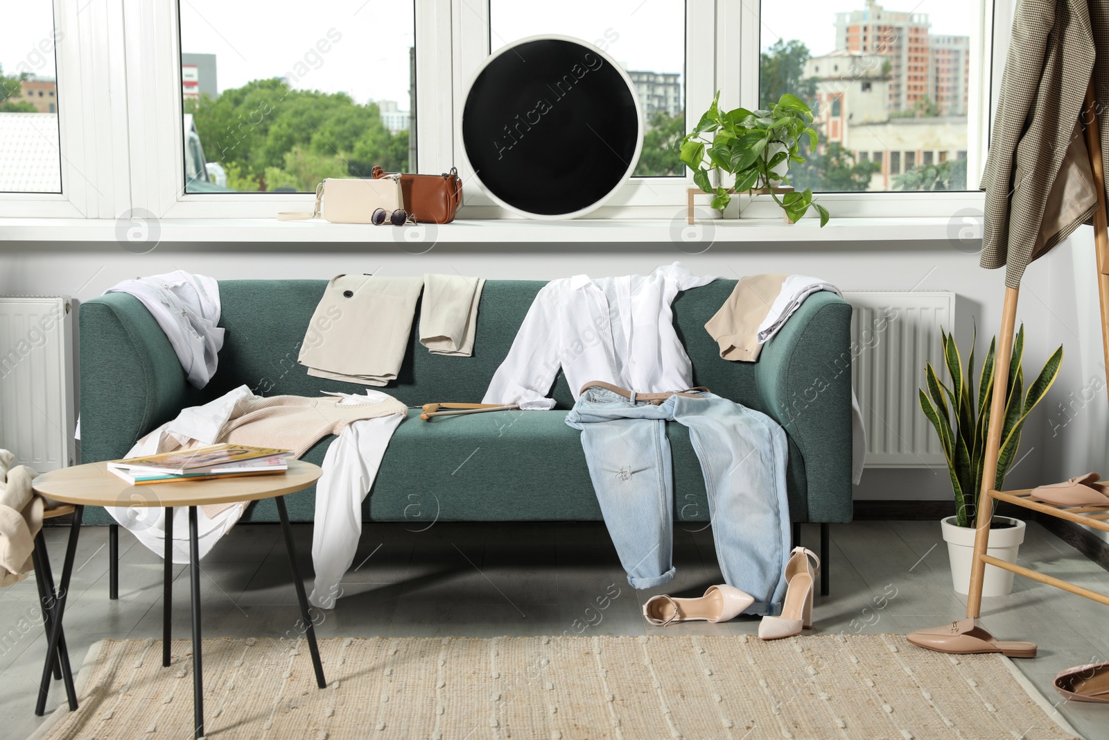 Photo of Messy pile of clothes on sofa and shoes in living room