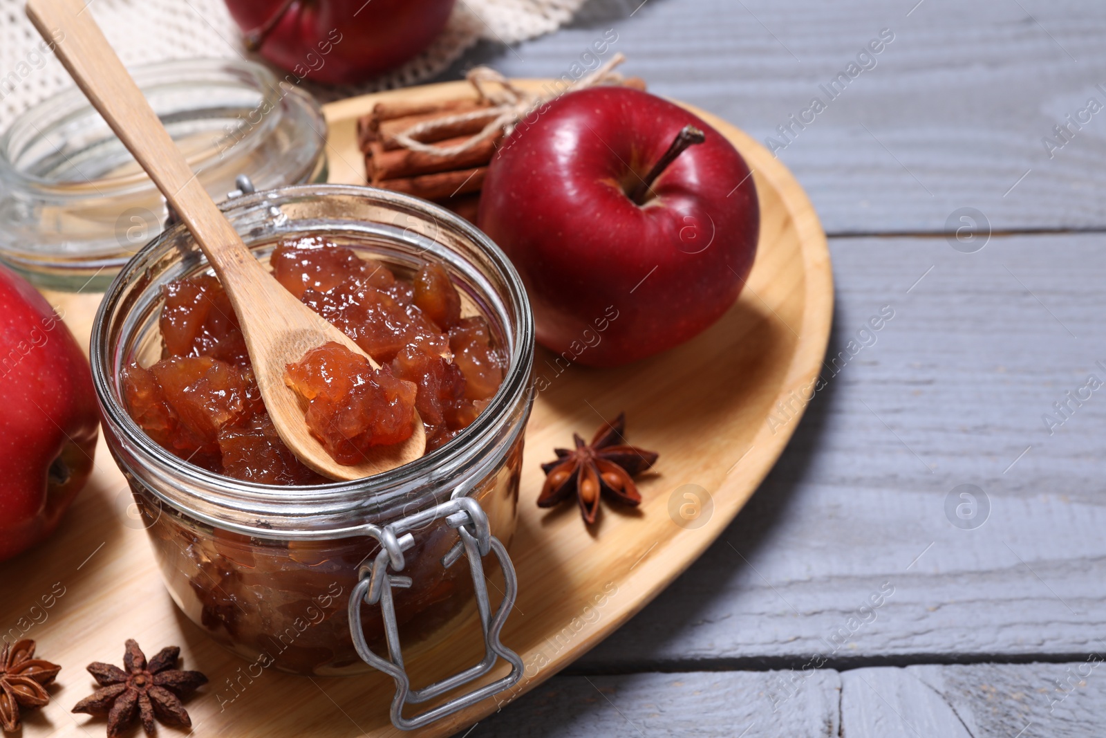 Photo of Delicious apple jam in jar, fresh fruits and spices on grey wooden table. Space for text