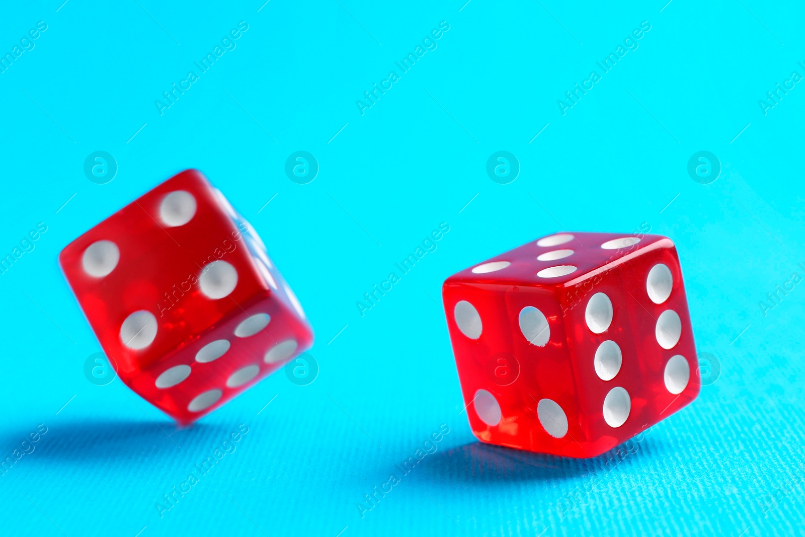 Photo of Two red game dices falling on light blue background, closeup