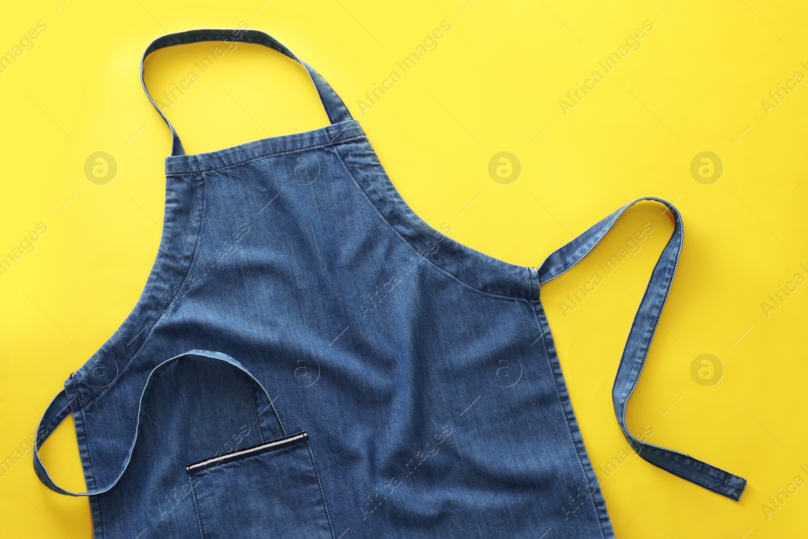 Photo of Denim blue kitchen apron on yellow background, top view