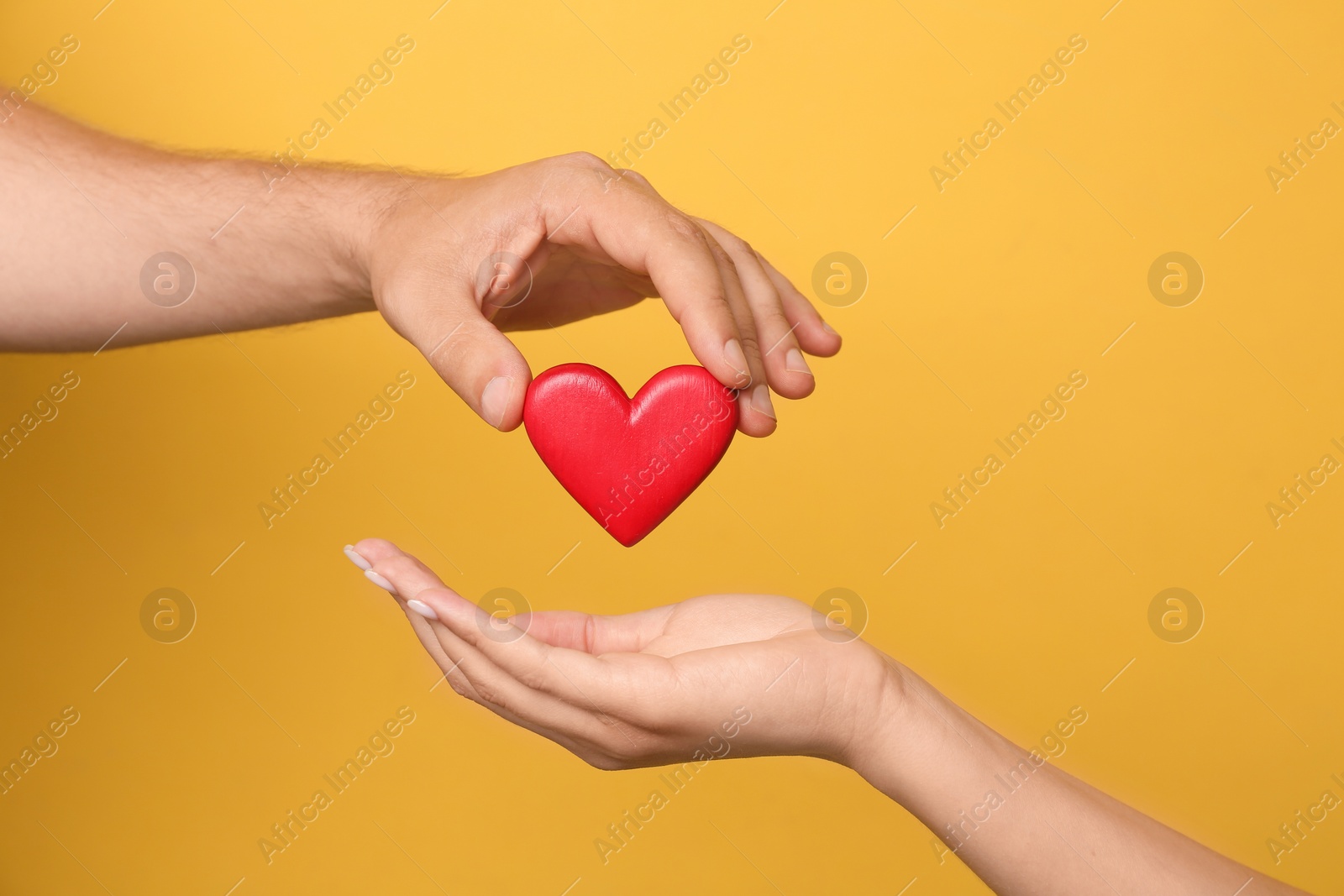 Photo of Man giving red heart to woman on yellow background, closeup. Donation concept