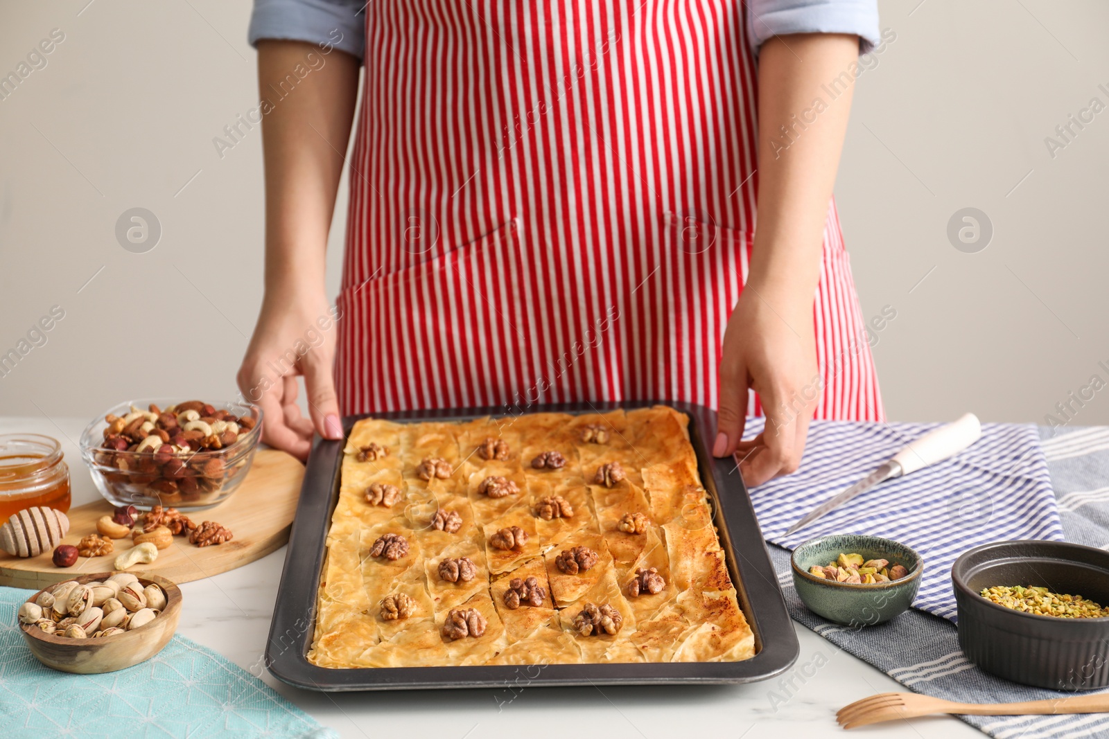 Photo of Woman with baking pan of delicious baklava at table, closeup