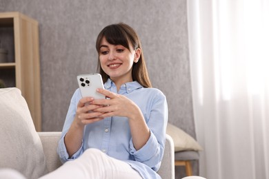 Photo of Beautiful young housewife using smartphone on sofa at home