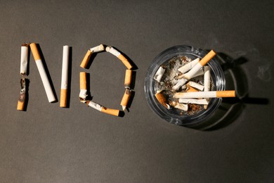 Word No made with burnt cigarettes and ashtray on black table, flat lay. Stop smoking concept