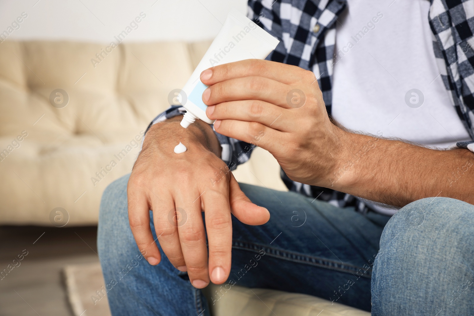 Photo of Man applying cream from tube onto hand indoors, closeup