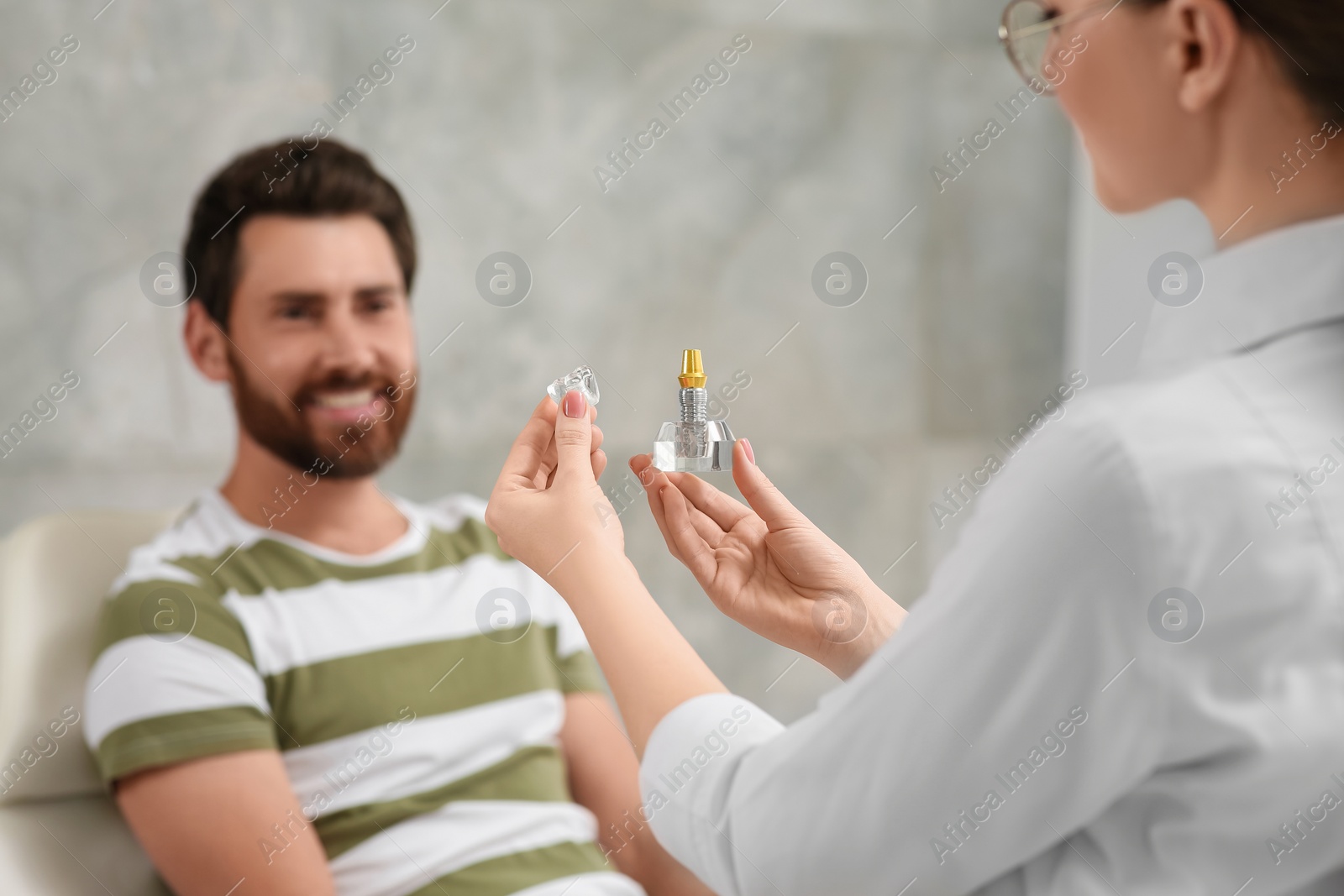 Photo of Doctor with educational model of dental implant consulting patient in clinic, closeup