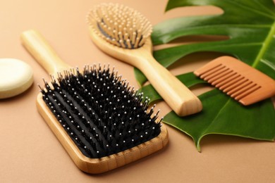 Photo of Wooden hairbrushes, comb, solid shampoo and green leaf on light brown background