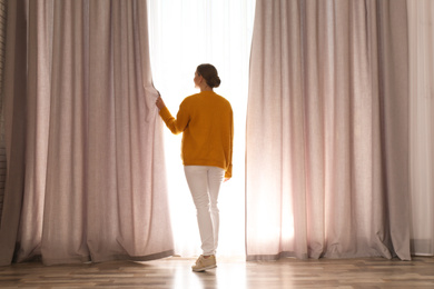 Woman near window with beautiful curtains at home in morning