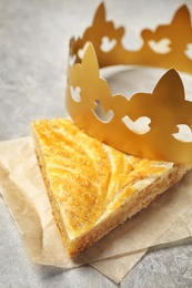 Photo of Slice of traditional galette des Rois with paper crown on light grey table, closeup