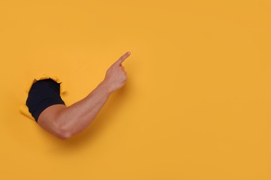 Photo of Special promotion. Man pointing at something through hole in orange paper, closeup. Space for text