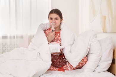 Cute girl using nebulizer for inhalation on bed at home