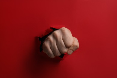 Photo of Man breaking through red paper with fist, closeup