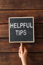 Image of Woman holding chalkboard with phrase Helpful Tips on wooden background, closeup