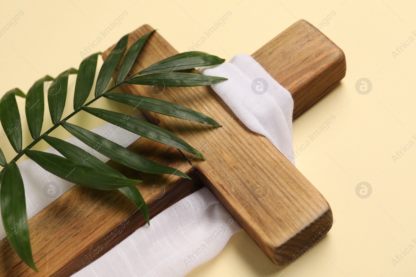 Photo of Wooden cross, white cloth and palm leaf on beige background, closeup. Easter attributes