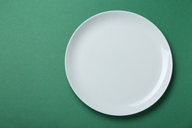 Empty white ceramic plate on green background, top view. Space for text
