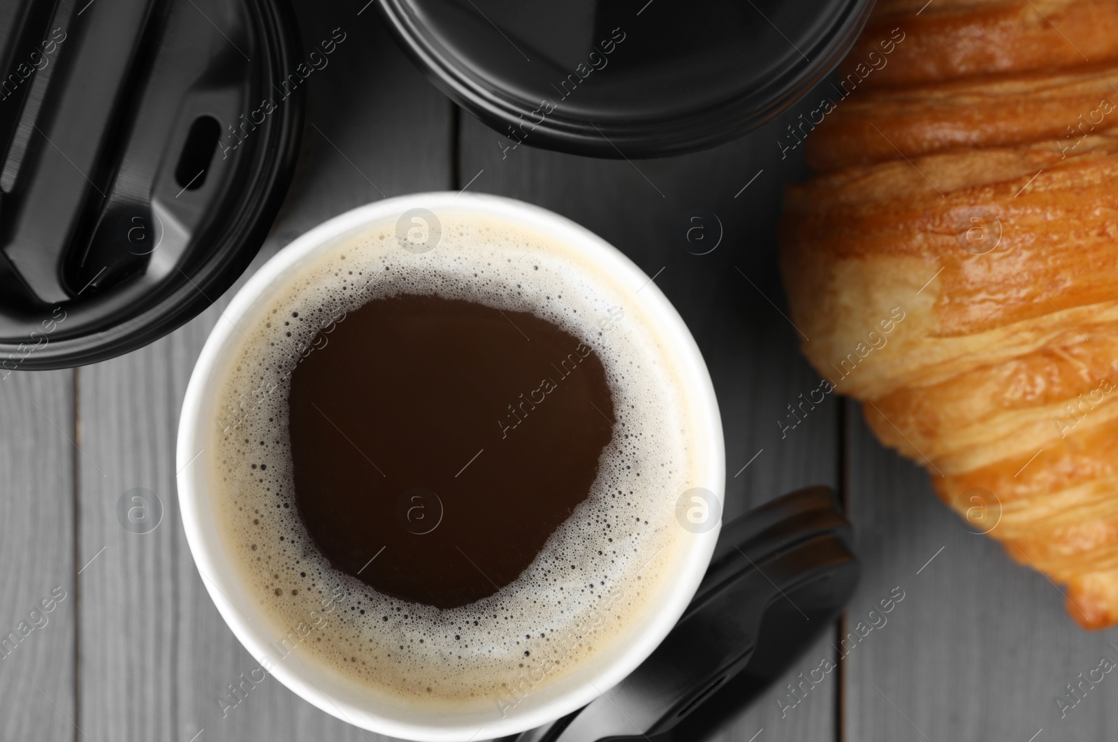 Photo of Coffee to go. Paper cups with tasty drink and croissant on grey wooden table, flat lay