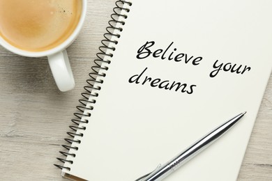 Image of Motivational quote Believe Your Dreams written in notebook on wooden table, flat lay