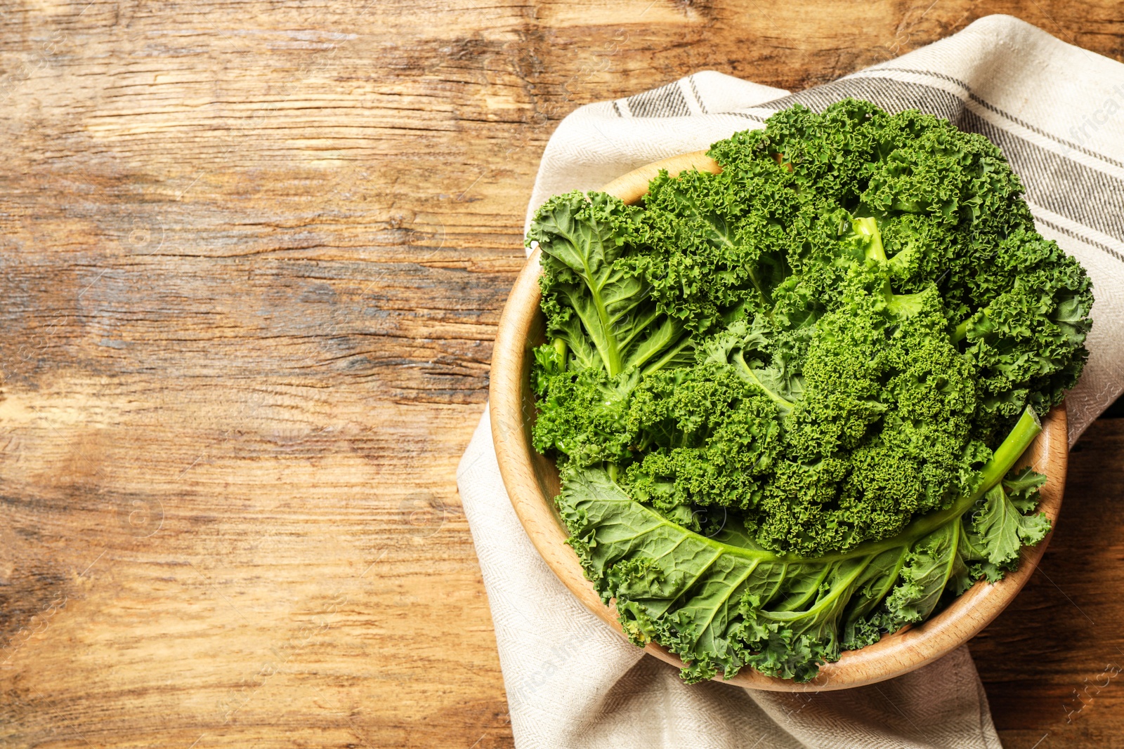 Photo of Fresh kale leaves on wooden table, top view. Space for text