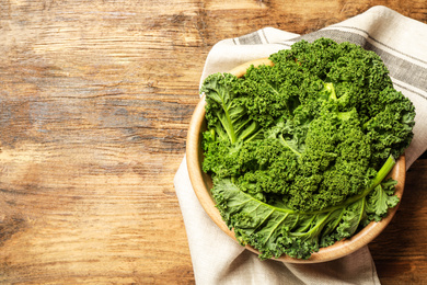 Photo of Fresh kale leaves on wooden table, top view. Space for text