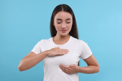 Photo of Beautiful woman doing breast self-examination on light blue background