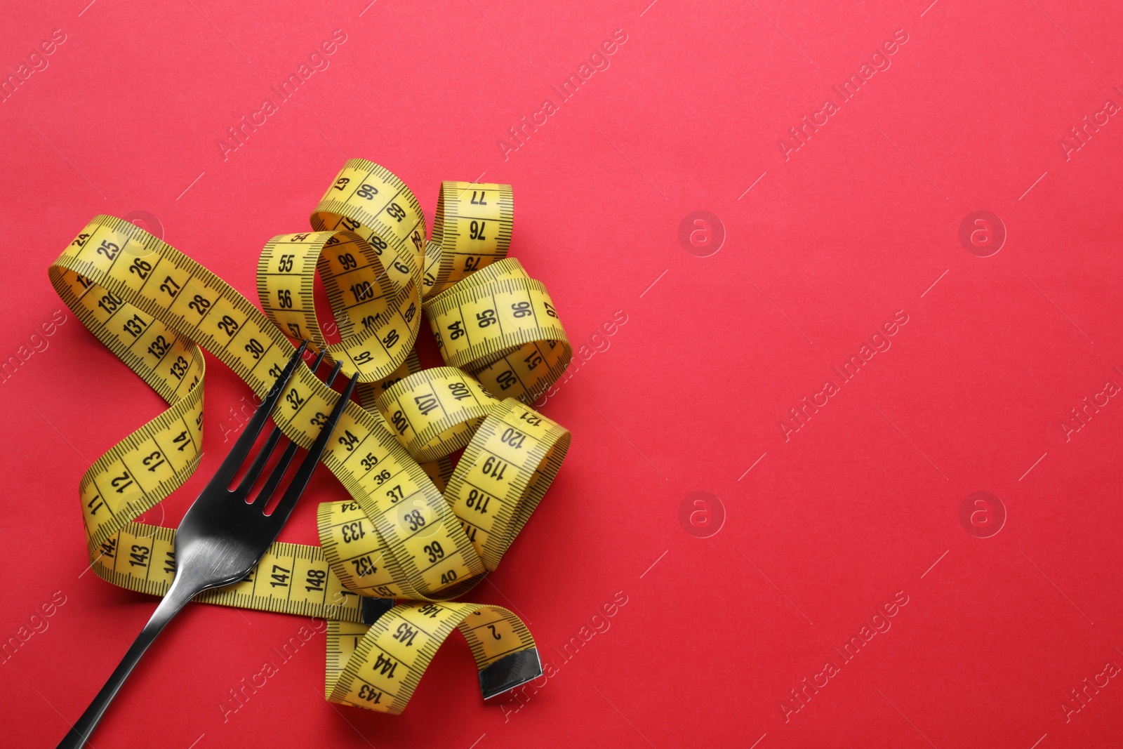 Photo of Fork with measuring tape on red background, top view and space for text. Diet concept