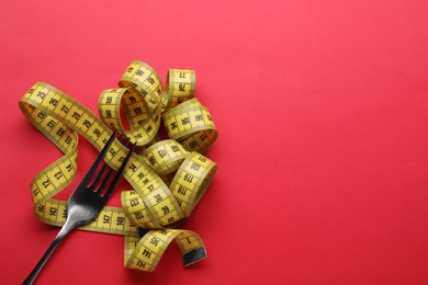 Photo of Fork with measuring tape on red background, top view and space for text. Diet concept