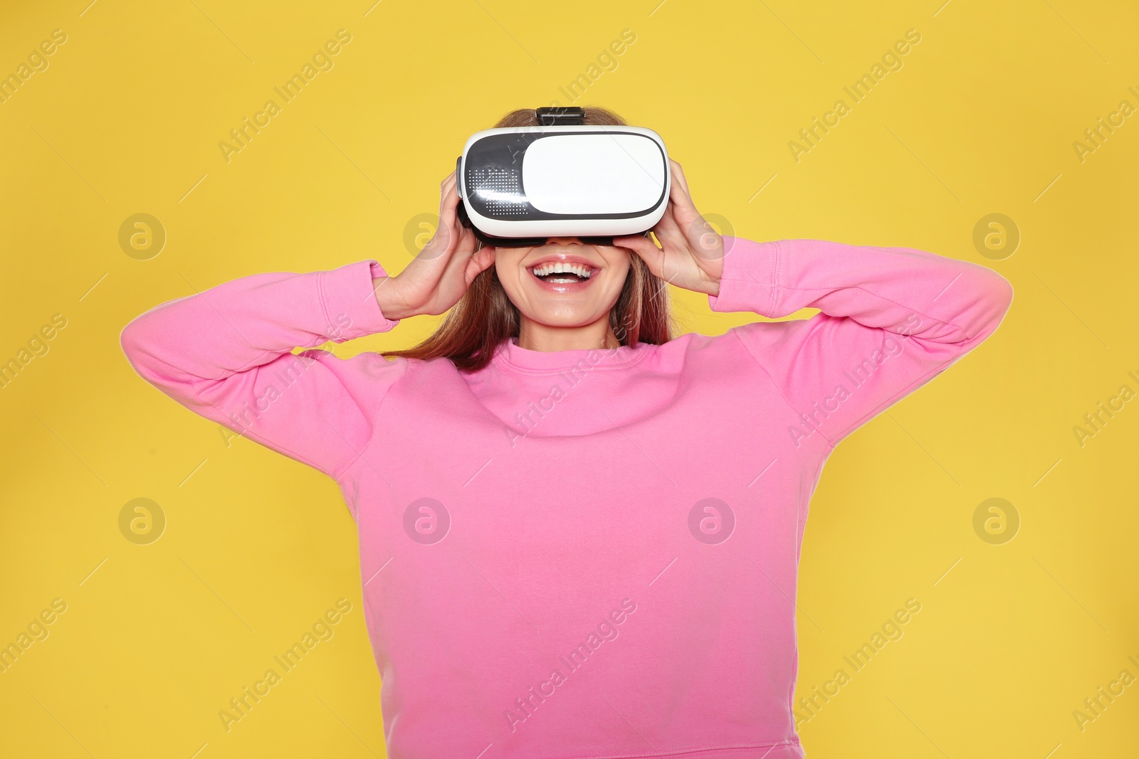 Photo of Emotional young woman playing video games with virtual reality headset on color background