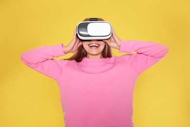 Photo of Emotional young woman playing video games with virtual reality headset on color background