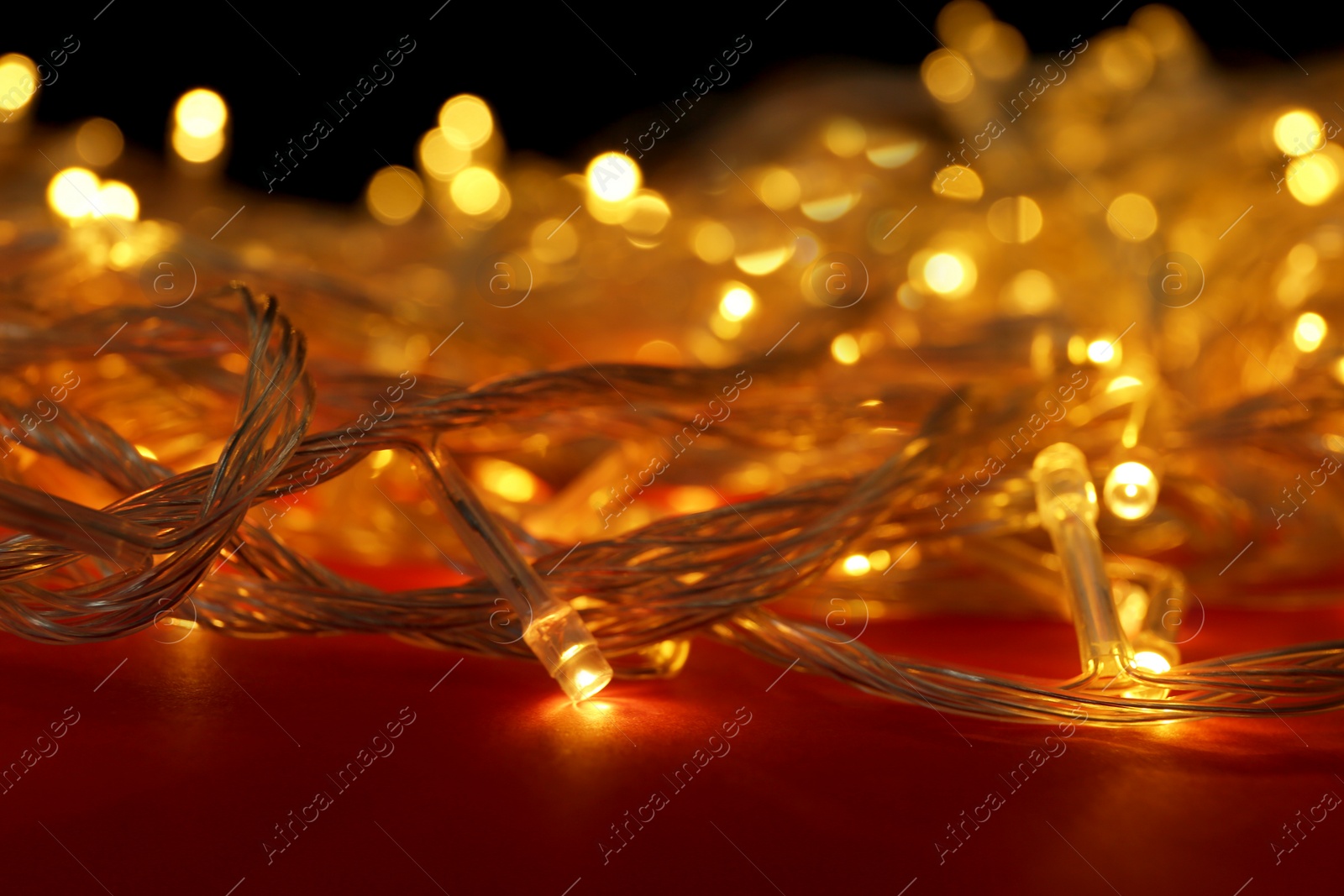 Photo of Glowing Christmas lights on red background, closeup