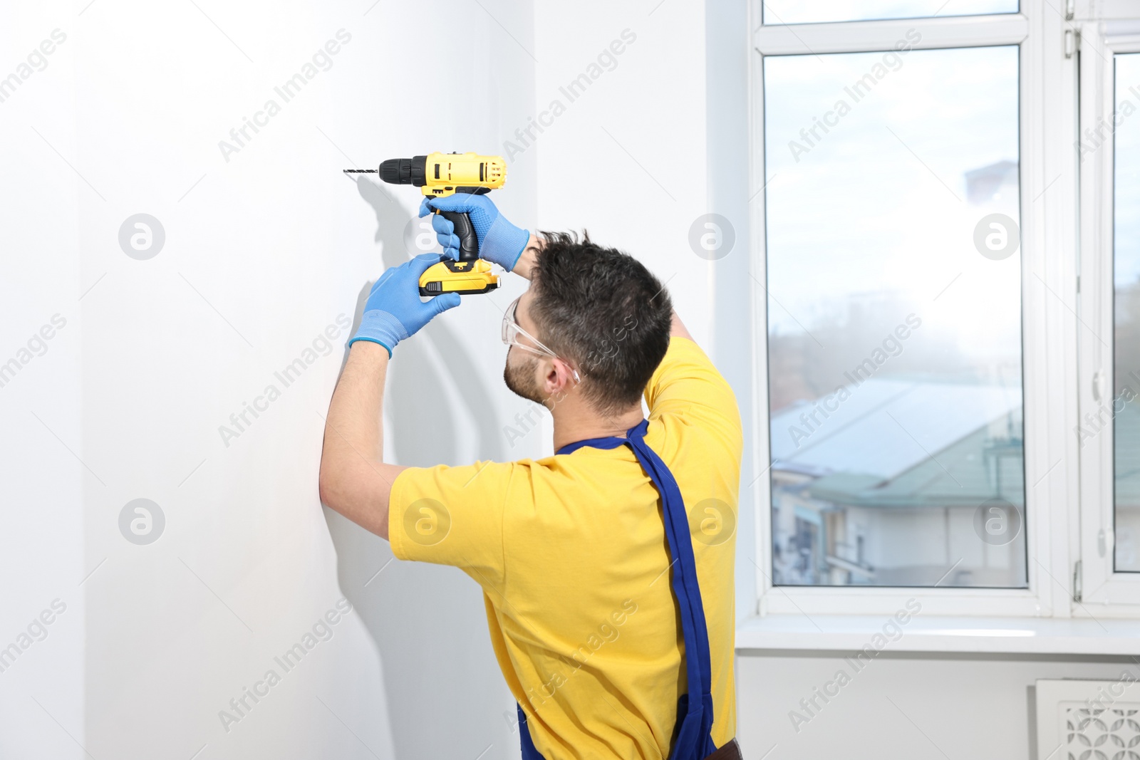 Photo of Young worker using electric drill indoors. Space for text