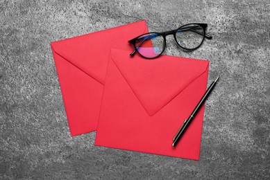 Red envelopes, glasses and pen on grey table, top view